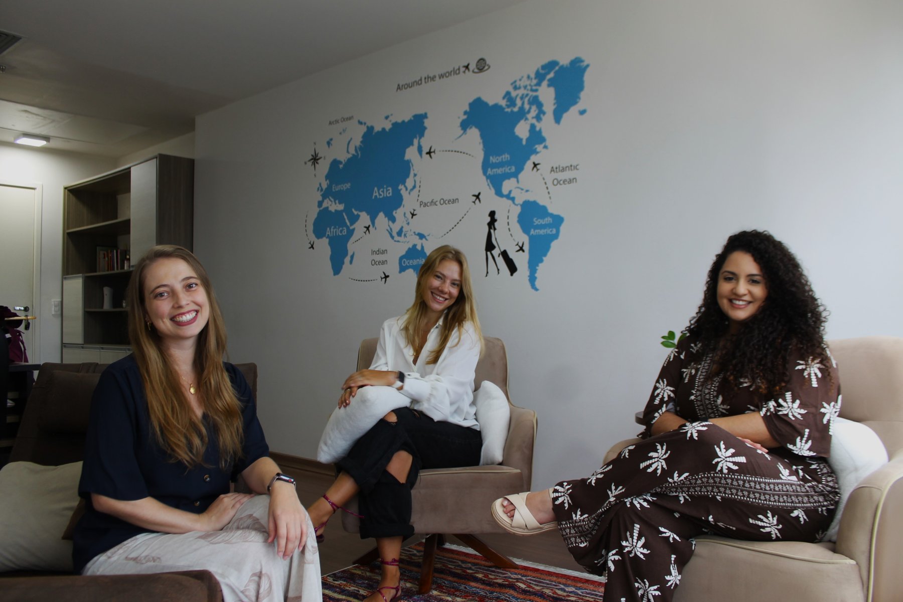 Profissionais da Serenitah sentadas na sala de atendimento, com um mapa-múndi na parede ao fundo